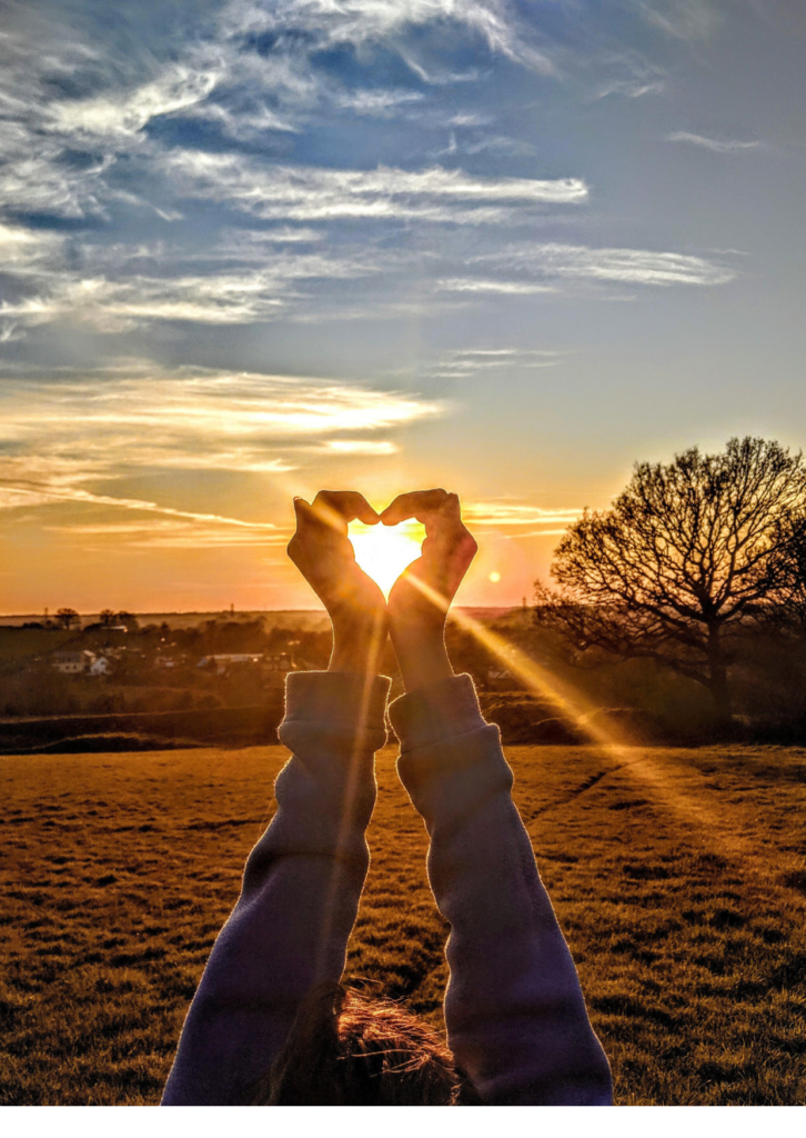Woman making heart shape with her hands to frame the sun