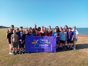 Mayor of Great Yarmouth, Cllr Jade Martin with staff and young carers from Caring Together Charity's Great Yarmouth and Gorleston Young Carers service stood behind a Caring Together Charity banner on Gorleston beach. 